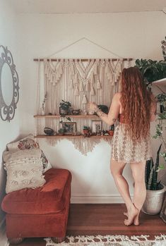 a woman standing in front of a shelf with plants on top of it next to a red couch