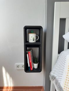 a shelf with books and coffee cups on it next to a white bed in a bedroom