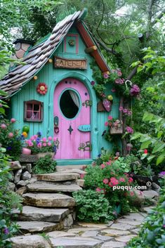 a pink and blue fairy house surrounded by greenery with steps leading up to it