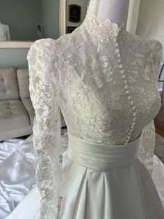 the back of a wedding dress on display in a room with white sheets and pillows