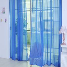 a chair sitting in front of a window with blue sheer curtains on the windowsill