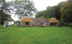 a house in the middle of a green yard with trees and people standing around it