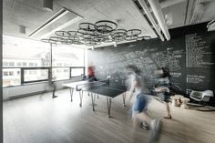 two people are playing ping pong in an office with blackboard walls and wooden floors