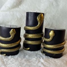 three candles with gold snakes on them sitting on a white furnishing area next to each other