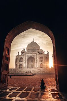 a person sitting on the ground in front of a building with an archway leading to it