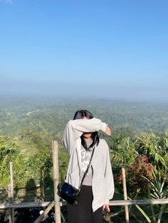 a woman standing on top of a lush green hillside holding her hands to her head