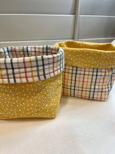 two small baskets sitting on top of a counter next to each other, one has a yellow and white checkered pattern