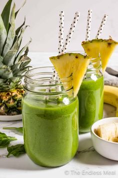 two mason jars filled with green smoothie and topped with pineapple slices