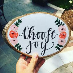 a hand holding up a wooden sign that says, choose joy with flowers on it