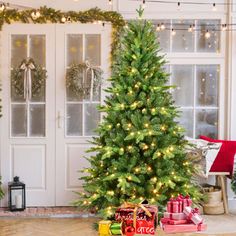 a decorated christmas tree in front of a white door with lights and presents on the floor