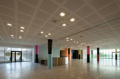 an empty room with large windows and colorful columns on the ceiling is lit by recessed lights