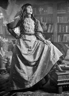 a woman sitting on top of a chair next to a book shelf