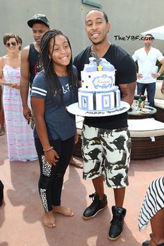 a man and woman holding a birthday cake in front of other people at an outdoor event