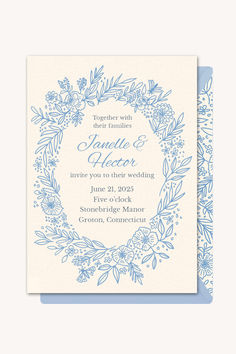 a blue and white wedding card with an ornate wreath design on the front, in light blue