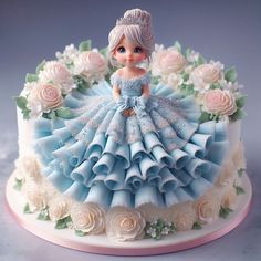 a cake with a doll on top of it and flowers around the edges that are white and blue