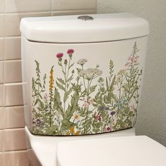 a white toilet sitting in a bathroom next to a tiled wall with flowers painted on it