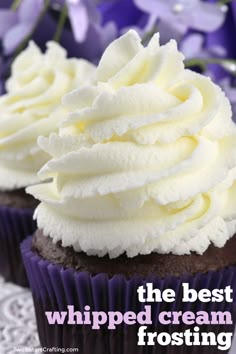 two cupcakes with white frosting sitting on a doily next to purple flowers