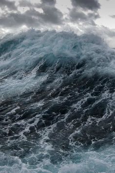 an ocean wave crashing into the shore under a cloudy sky