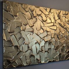 an abstract painting with gold and silver paint on the wall in front of a gray wall