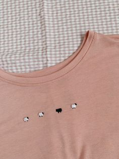 three black and white sheep embroidered on the back of a pink t - shirt with gingham background