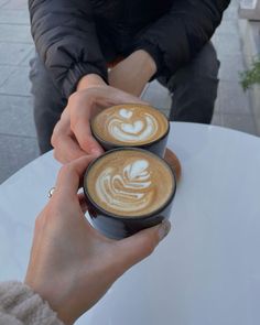 two people sitting at a table with cups of coffee in front of them, both holding their hands together