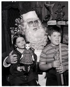 black and white photograph of santa claus with two children in front of him holding a toy