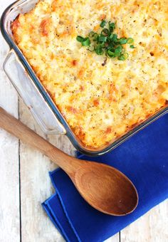 a casserole with cheese and green onions in a glass dish next to a wooden spoon