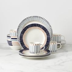 a set of blue and white striped dishes on a marble countertop with matching cups