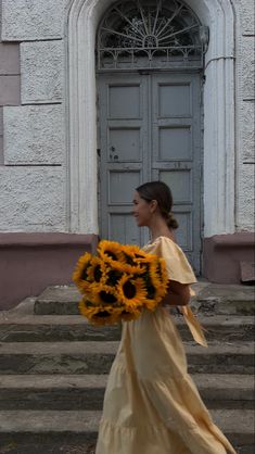 a woman is walking down the street with a bouquet of sunflowers in her hand