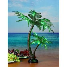 a small palm tree next to a plate of grapes and grapes on a table with the ocean in the background