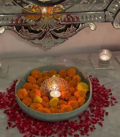 a bowl filled with orange flowers and a lit candle on top of a white table