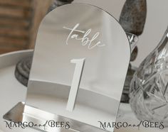 a table number is placed on top of a silver plate with glass vases in the background