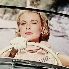 a woman sitting in the driver's seat of a car with her hand on the steering wheel