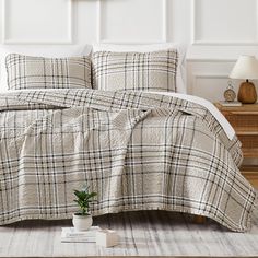 a bed with plaid comforter and pillows on top of it, next to a small potted plant