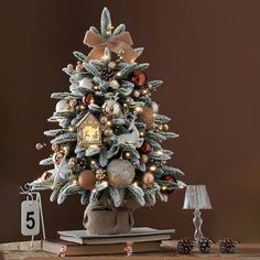 a small christmas tree with ornaments and lights on it's base, next to a clock