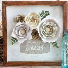 some paper flowers in a wooden frame on a shelf next to a mason jar and glass bottle