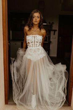 a woman in a white wedding dress is standing by an open door and looking at the camera