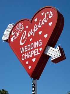 a large red heart shaped sign with white hearts on it's sides that says cupid wedding chapel