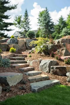 a rock garden with steps leading up to the house and trees in the back ground