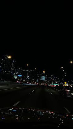 the city lights shine brightly in the dark night time sky over an empty highway with cars driving on it