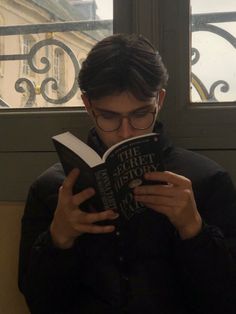 a young man reading a book in front of a window