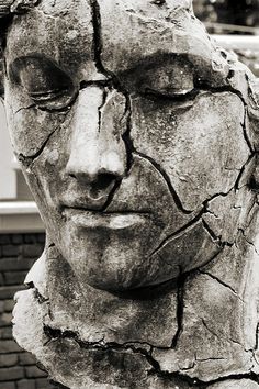 a black and white photo of a face made out of cracked up concrete with trees in the background