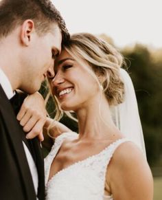 a bride and groom smile at each other as they pose for a wedding photo together