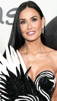 a woman in a black and white dress with feathers on her chest posing for the camera