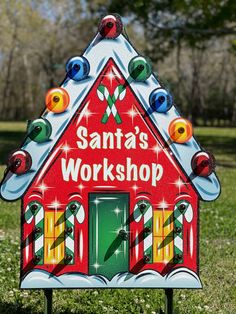 a santa's workshop sign in the grass with candy canes around it and lights on top