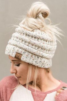 a woman with blonde hair wearing a white knitted beanie and looking down at her phone