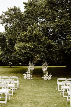 an outdoor ceremony setup with white chairs and flowers on the aisle, surrounded by trees