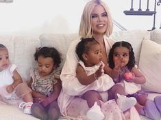 a woman sitting on top of a white couch with three small children in front of her