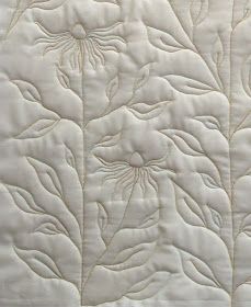 a close up view of a white quilted material with flowers and leaves on it