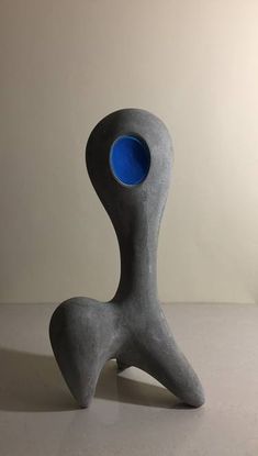 a gray sculpture with a blue hole in the center on a table top next to a white wall